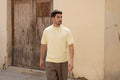 Man walking past a weathered wooden door in a Freedom Fit Tee in Butter Yellow with brown pleated trousers