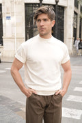 Man on a street corner in an off-white Freedom Fit Tee with rolled-up sleeves and brown pleated trousers